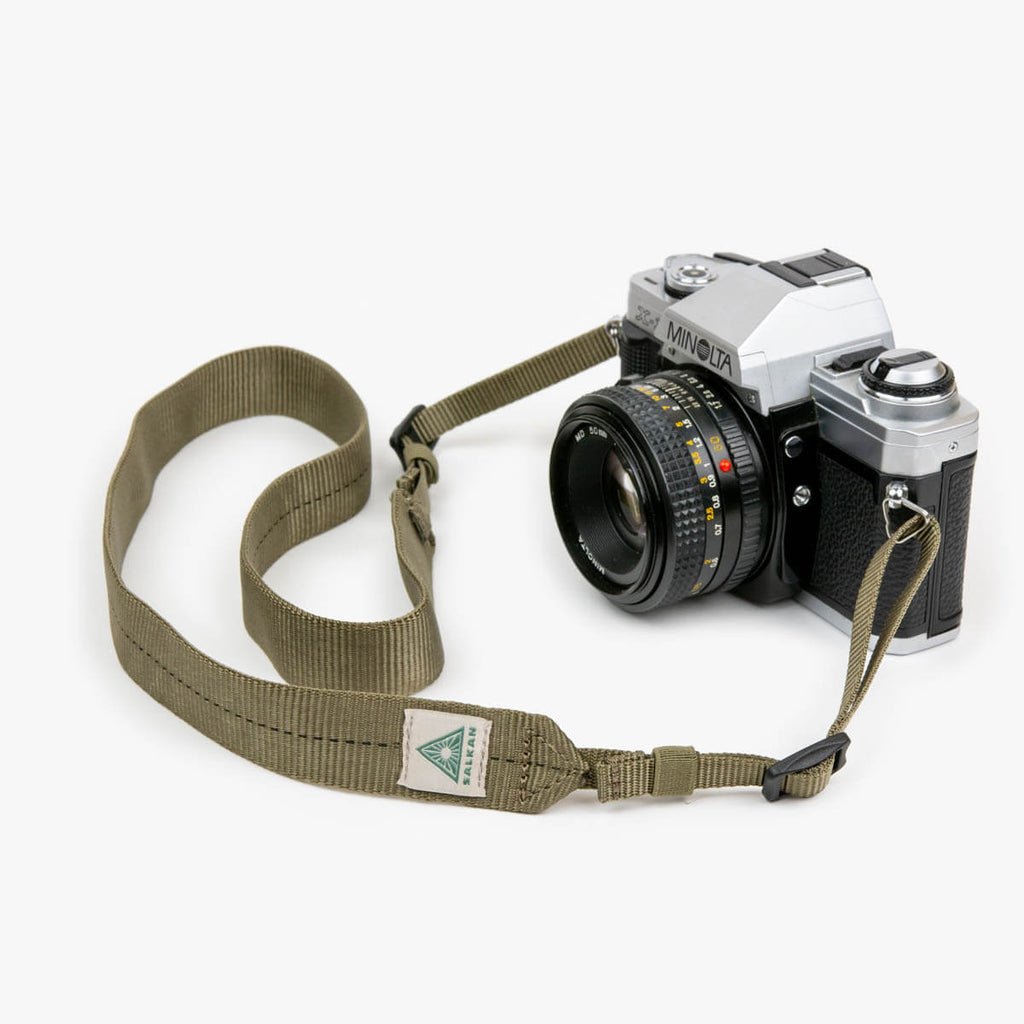 Salkan camera strap in olive green, coiled beside a vintage Minolta film camera